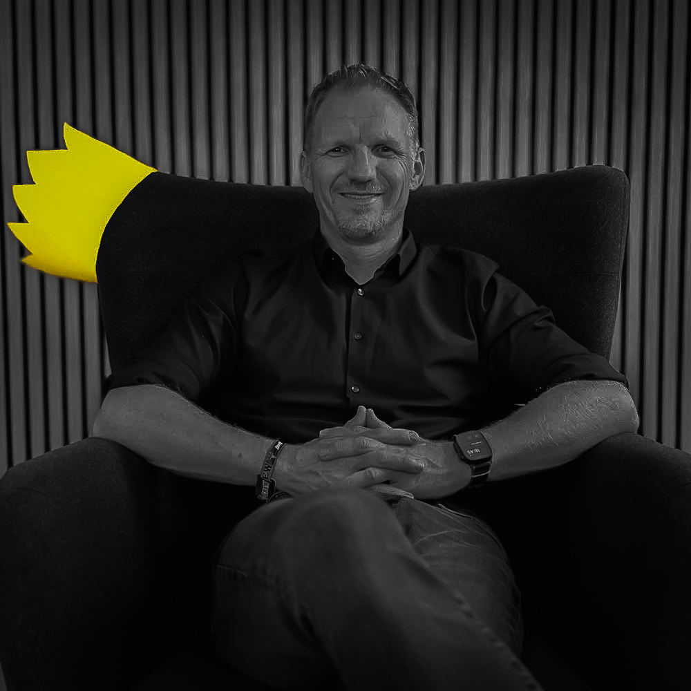 Timo Koenig sitzt entspannt in einem Sessel, hinter ihm eine gelbe Papierkrone
